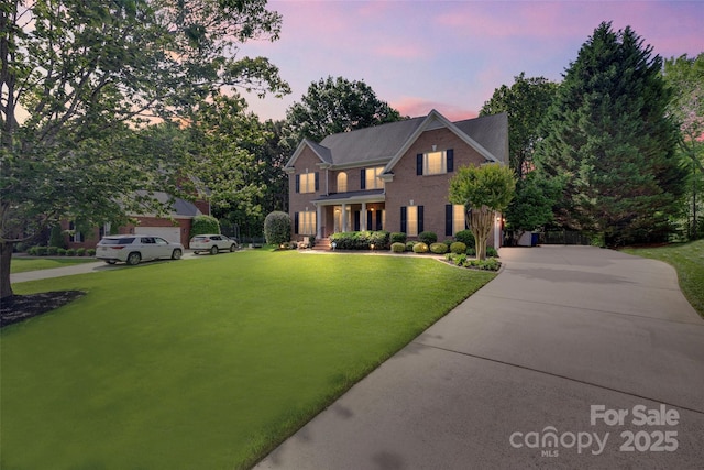 view of front of home with a yard, brick siding, and concrete driveway
