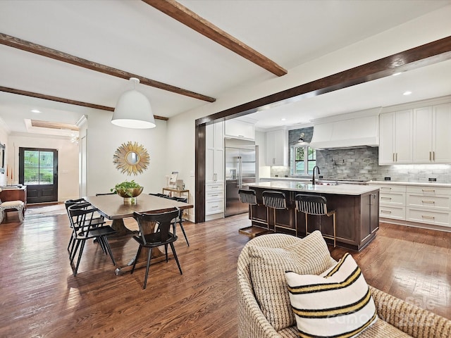 kitchen featuring built in fridge, light countertops, custom range hood, decorative backsplash, and white cabinetry
