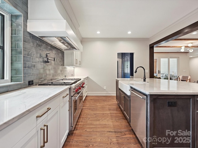 kitchen featuring premium range hood, stainless steel appliances, a sink, backsplash, and light wood-style floors