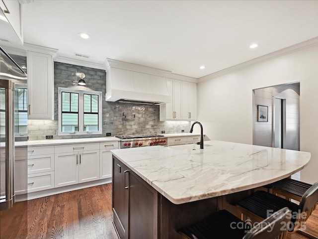 kitchen with a sink, custom range hood, ornamental molding, a kitchen bar, and dark wood-style flooring