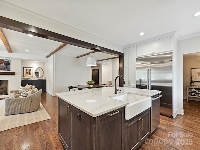 kitchen with a sink, open floor plan, appliances with stainless steel finishes, dark brown cabinetry, and beamed ceiling