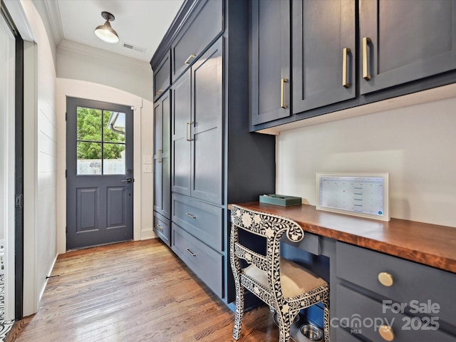 mudroom featuring built in study area, light wood finished floors, and ornamental molding