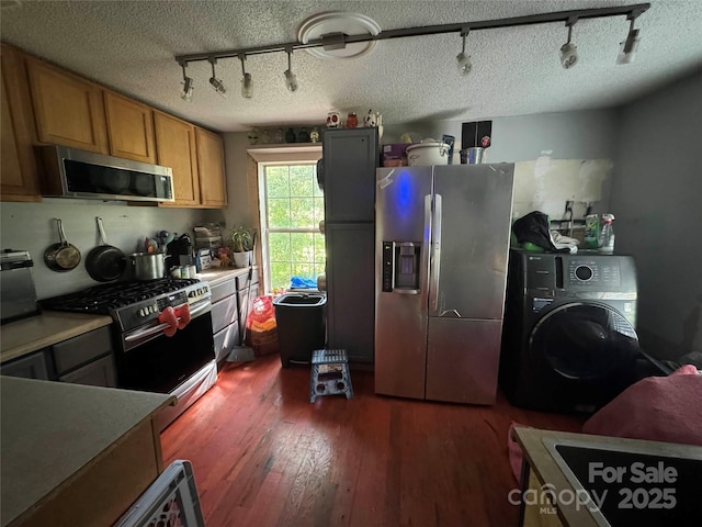 kitchen with stainless steel appliances, track lighting, washer / dryer, dark wood-style flooring, and brown cabinetry