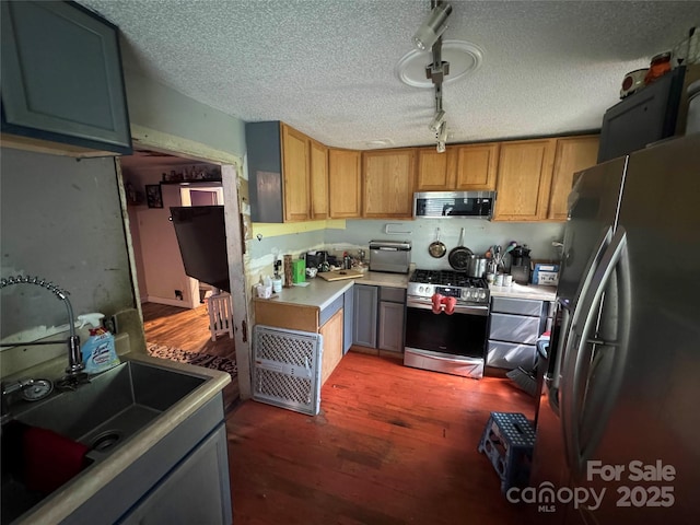 kitchen featuring stainless steel appliances, a sink, track lighting, a textured ceiling, and light countertops