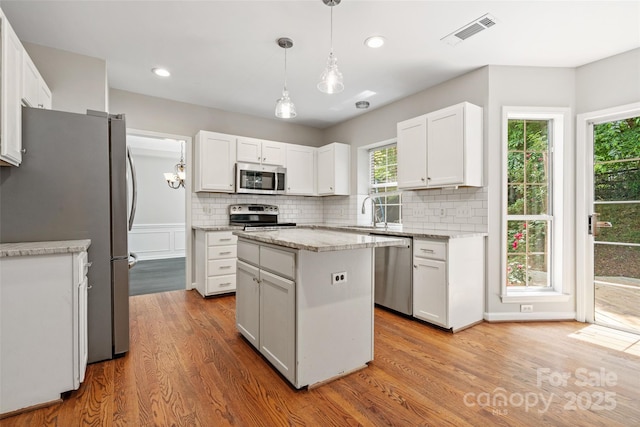 6434 Skyline Dr, Charlotte, NC 28269 - kitchen featuring stainless steel appliances, light wood-type flooring, tasteful backsplash, white cabinetry, and a center island
