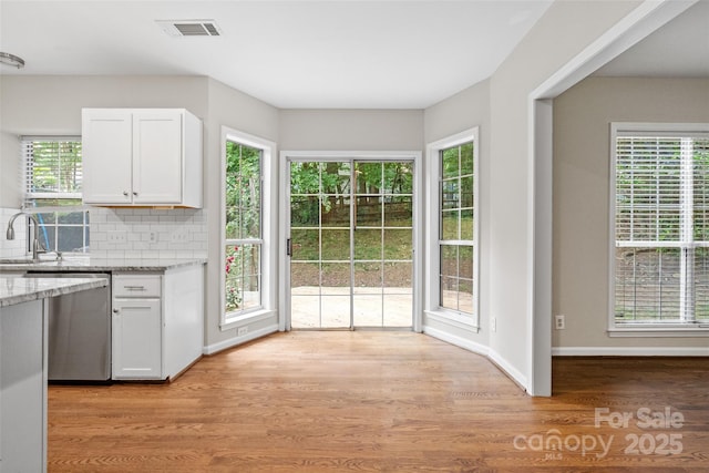 6434 Skyline Dr, Charlotte, NC 28269 - kitchen with stainless steel dishwasher, white cabinetry, light stone counters, light wood-type flooring, and tasteful backsplash