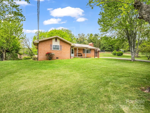rear view of house featuring brick siding, a chimney, a yard, covered porch, and crawl space