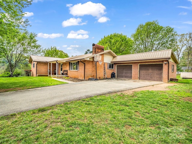 single story home featuring driveway, an attached garage, a chimney, a front yard, and brick siding