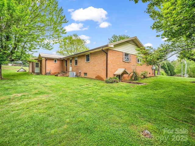 rear view of property with a yard, brick siding, and central AC