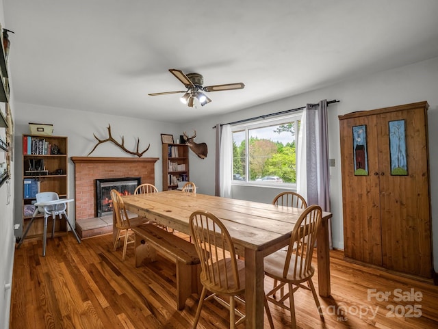 dining space featuring a brick fireplace, ceiling fan, and wood finished floors