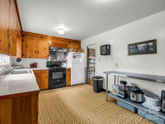 kitchen featuring black electric range oven, freestanding refrigerator, a sink, under cabinet range hood, and light countertops