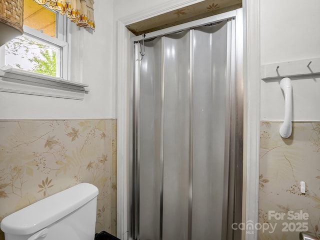 bathroom with wallpapered walls, toilet, and a shower