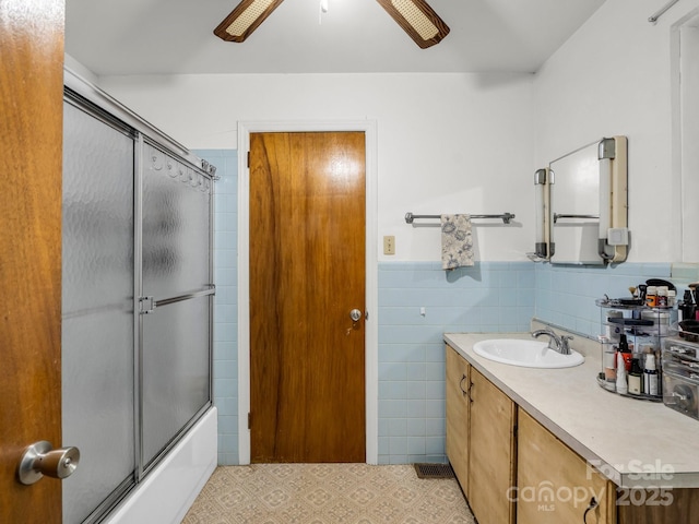 bathroom with ceiling fan, tile walls, vanity, a wainscoted wall, and enclosed tub / shower combo