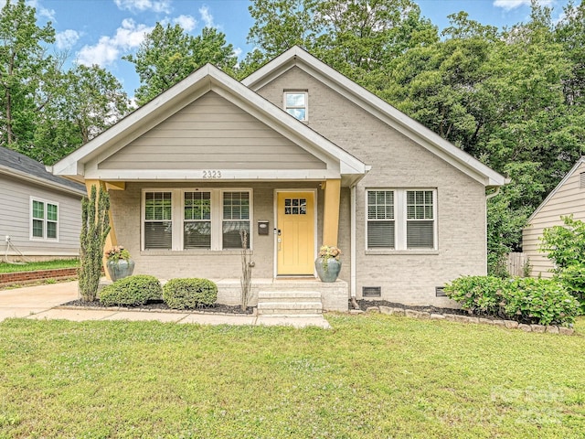bungalow-style home with a front yard, covered porch, and brick siding
