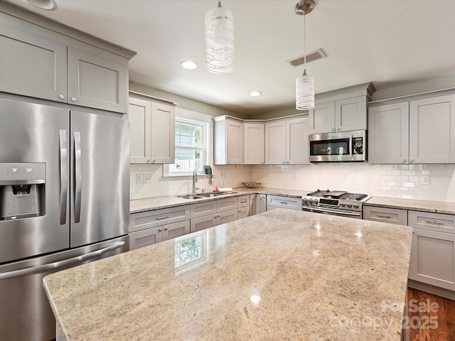 kitchen featuring appliances with stainless steel finishes, a sink, gray cabinets, backsplash, and light stone countertops