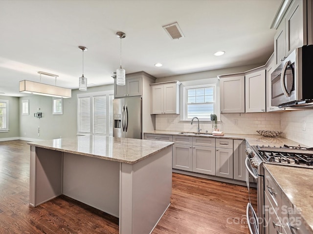 kitchen with appliances with stainless steel finishes, a sink, a kitchen island, light stone counters, and gray cabinets