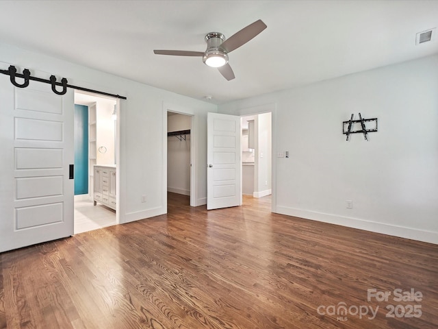 unfurnished bedroom with a barn door, wood finished floors, baseboards, and connected bathroom