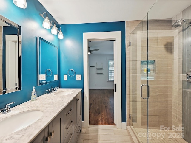 full bath featuring a shower stall, a ceiling fan, baseboards, and double vanity