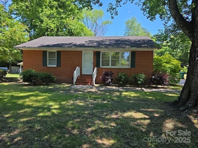 view of front of house featuring brick siding, a front yard, entry steps, and a shingled roof