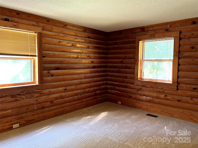 unfurnished room with carpet, log walls, a textured ceiling, and healthy amount of natural light