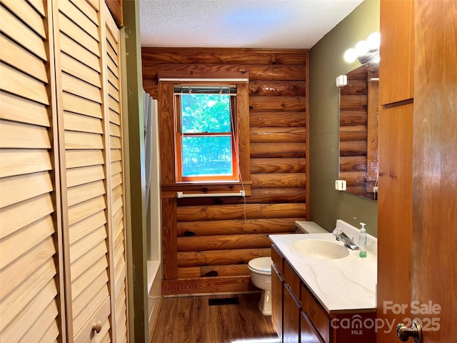 full bathroom featuring log walls, toilet, wood finished floors, vanity, and a textured ceiling