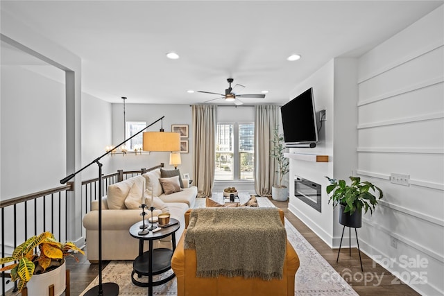 living area with recessed lighting, a ceiling fan, wood finished floors, a glass covered fireplace, and baseboards