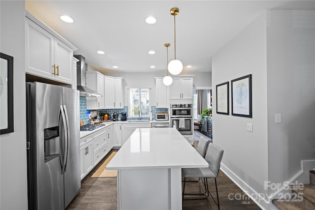 kitchen featuring stainless steel appliances, wall chimney exhaust hood, a center island, decorative backsplash, and a sink