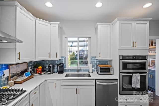 kitchen with stainless steel appliances, a sink, wall chimney exhaust hood, white cabinetry, and light countertops