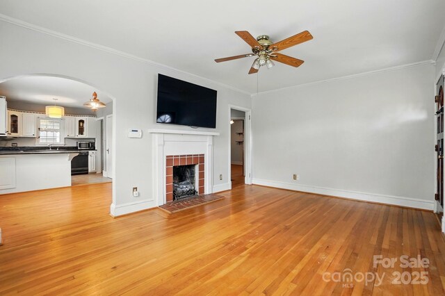 unfurnished living room featuring a tile fireplace, ornamental molding, light wood-style floors, and ceiling fan