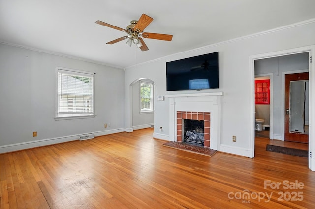 unfurnished living room featuring a ceiling fan, a fireplace, hardwood / wood-style floors, arched walkways, and ornamental molding