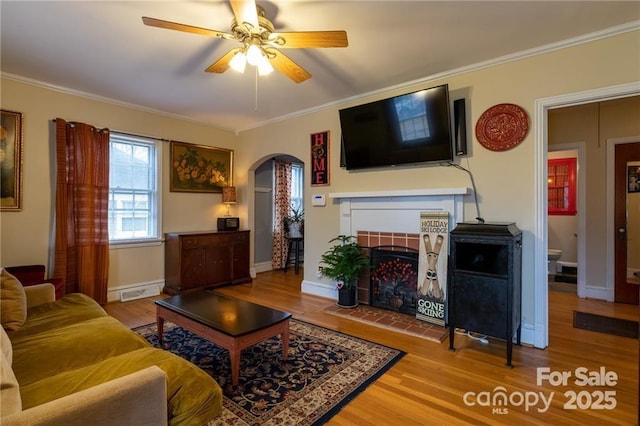 living room with arched walkways, wood finished floors, ornamental molding, a ceiling fan, and a tiled fireplace