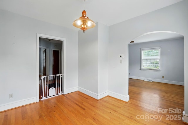 spare room featuring arched walkways, baseboards, visible vents, and light wood-style floors