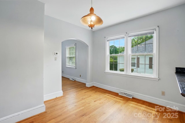 empty room featuring arched walkways, baseboards, light wood finished floors, and visible vents