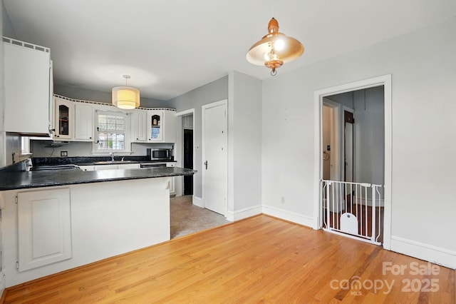 kitchen with glass insert cabinets, baseboards, a sink, stainless steel microwave, and dark countertops