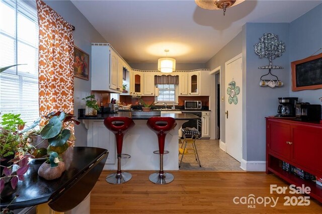 kitchen featuring stainless steel microwave, a peninsula, glass insert cabinets, a kitchen bar, and dark countertops