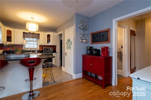 kitchen featuring stainless steel microwave, a kitchen bar, dark countertops, glass insert cabinets, and a peninsula