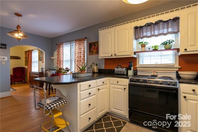 kitchen featuring black range, arched walkways, a peninsula, dark countertops, and white cabinets