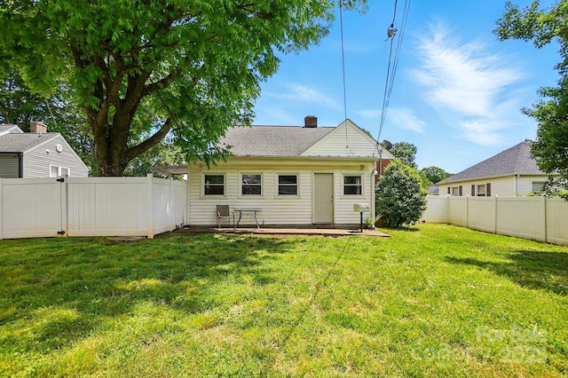 back of house with a yard, a chimney, and a fenced backyard