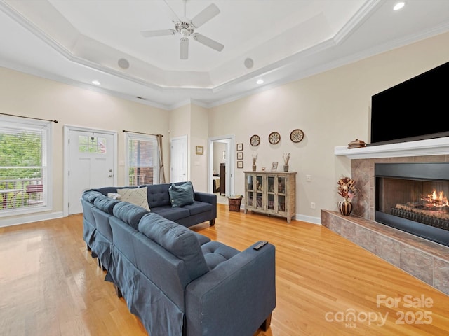 living room with a fireplace, a raised ceiling, a wealth of natural light, and light wood-type flooring