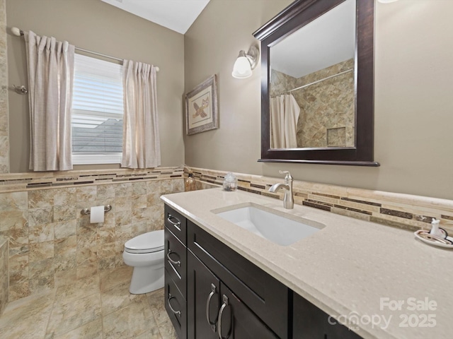 bathroom featuring tile walls, toilet, a shower with shower curtain, vanity, and a wainscoted wall