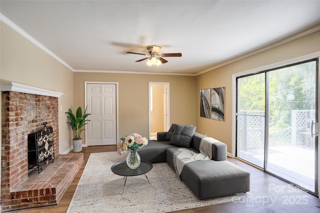 living area with a ceiling fan, wood finished floors, a brick fireplace, ornamental molding, and baseboards