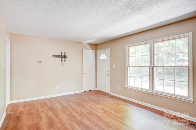 foyer entrance featuring light wood-style floors, a textured ceiling, and baseboards