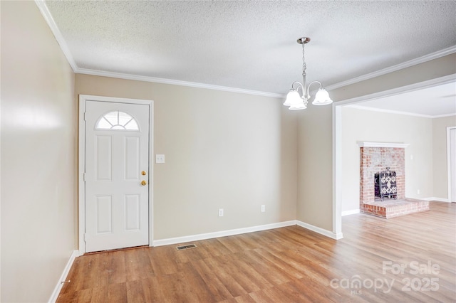 foyer entrance with wood finished floors, a textured ceiling, a chandelier, ornamental molding, and baseboards