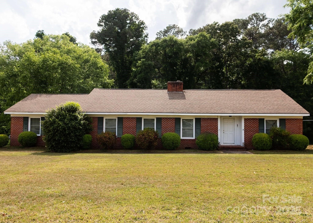 single story home featuring brick siding, a front lawn, and a chimney