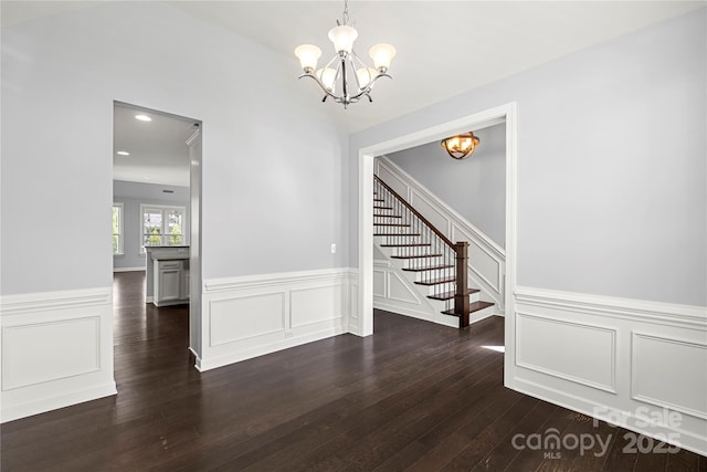 unfurnished dining area with a chandelier, wood-type flooring, stairway, a decorative wall, and wainscoting