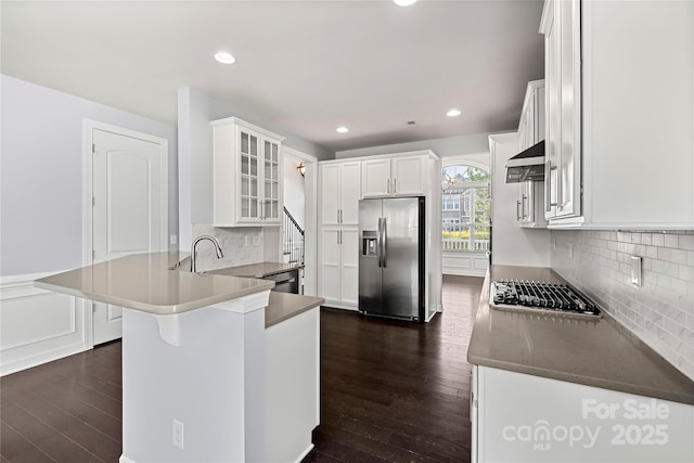 kitchen featuring appliances with stainless steel finishes, a peninsula, dark wood-style flooring, glass insert cabinets, and recessed lighting