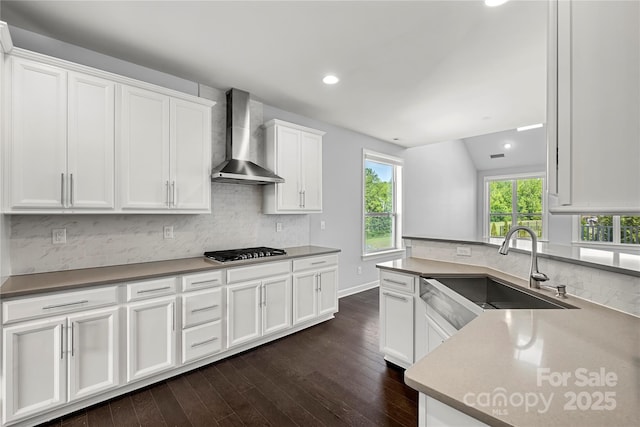 kitchen featuring wall chimney range hood, gas cooktop, dark wood-style floors, a sink, and white cabinets