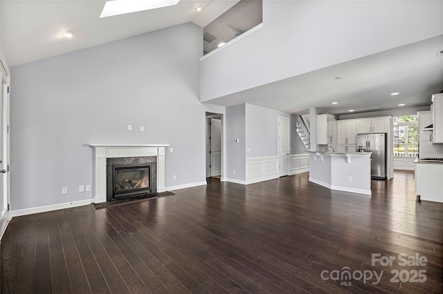 unfurnished living room with a fireplace, dark wood finished floors, stairway, high vaulted ceiling, and a skylight