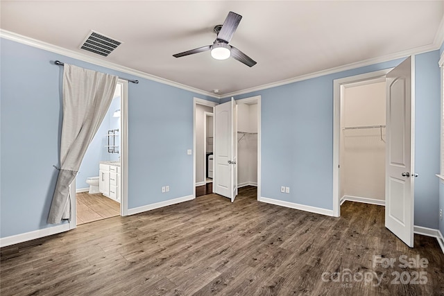 unfurnished bedroom with wood finished floors, ornamental molding, baseboards, and a spacious closet