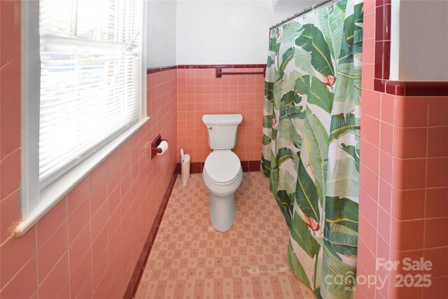 1101 Pee Dee Ave, Albemarle, NC 28001 - bathroom featuring tile patterned floors, tile walls, plenty of natural light, a wainscoted wall, and toilet